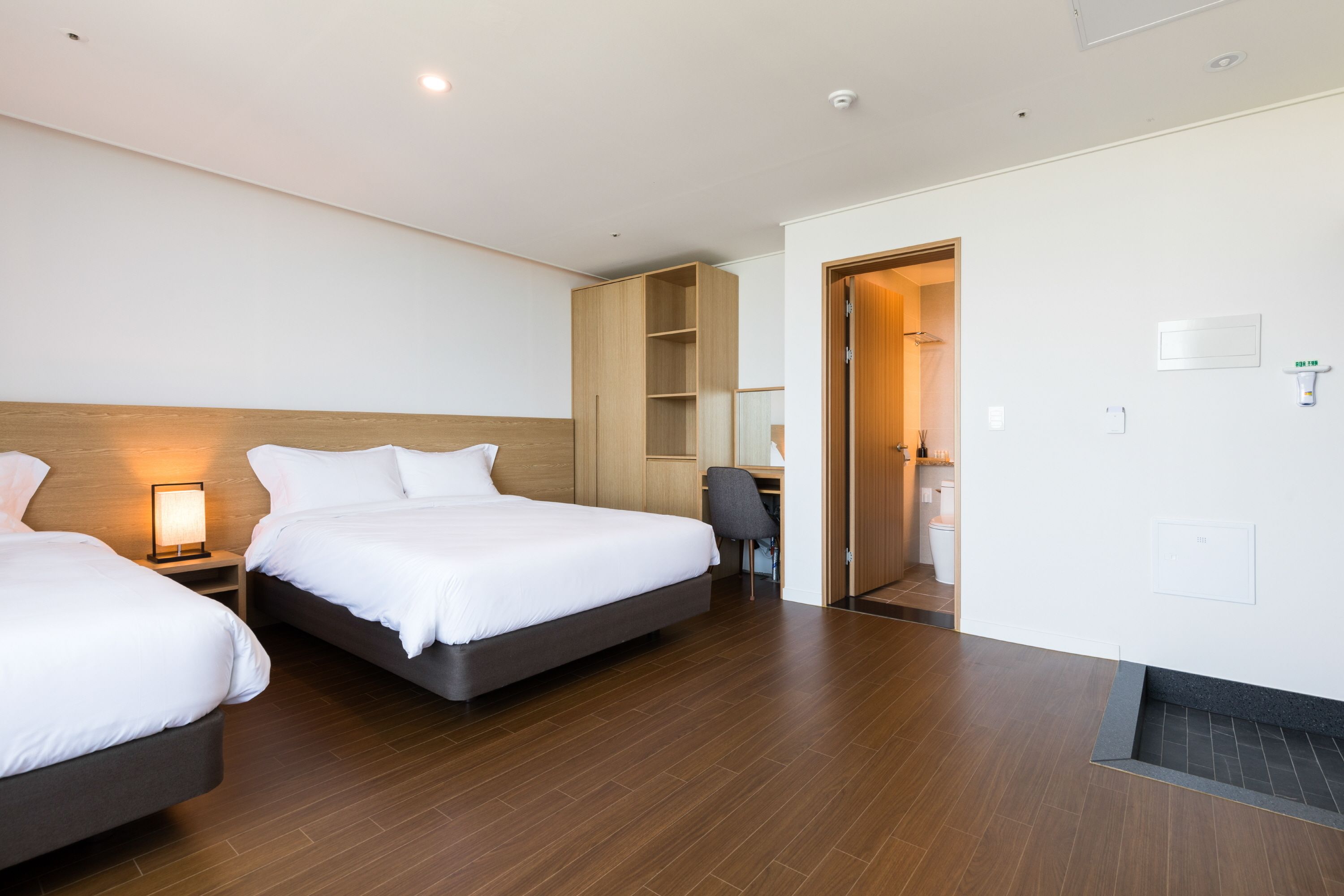 A hotel room with two beds, a desk, a chair, and a wardrobe.