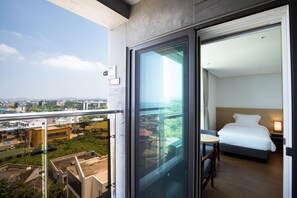 A hotel room with a balcony, a bed, a bedside table, and a view of the cityscape. - Lemain hotel (Jeju City)