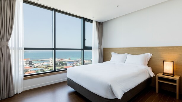 Habitación de hotel con un ventanal grande, una cama, una mesita de noche y vistas al mar.