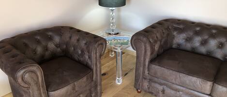 Two brown tufted armchairs facing each other with a small table and a lamp between them.