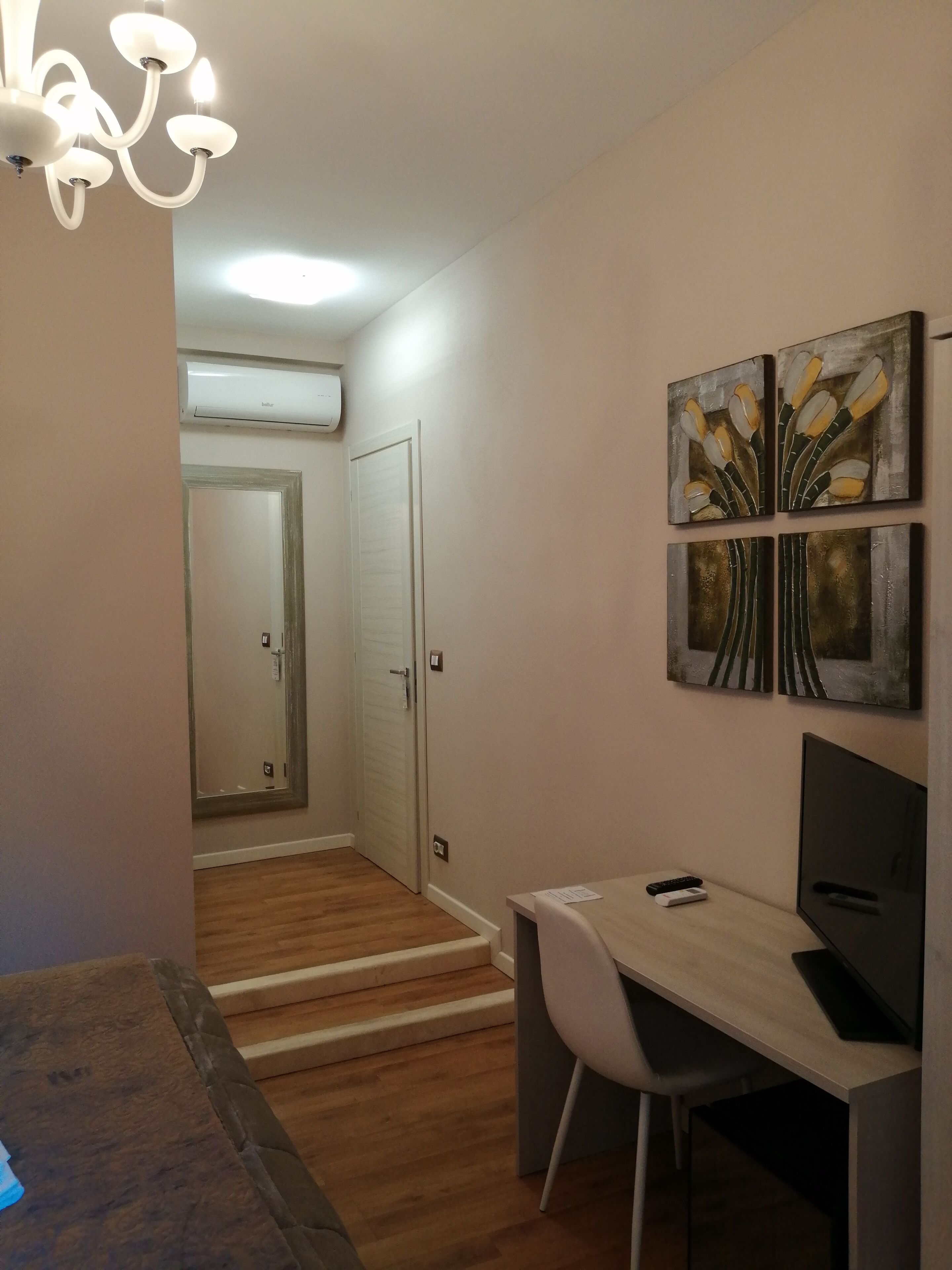A hallway with a wooden floor, a desk with a chair, a TV, and artwork on the wall.