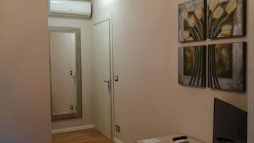 A hallway with a wooden floor, a desk with a chair, a TV, and artwork on the wall.