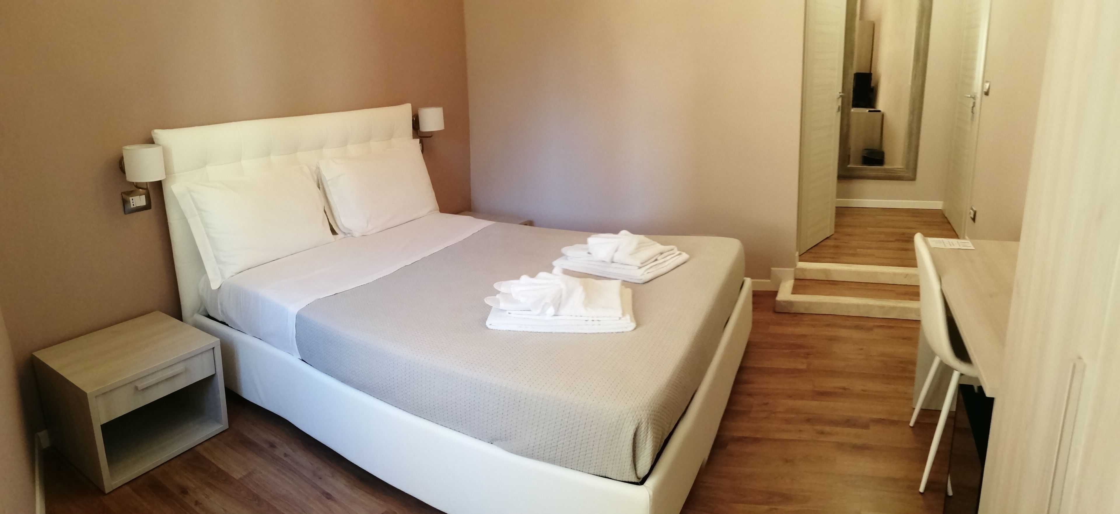 A neatly made bed with white linens and towels, a bedside table, and a wooden floor.