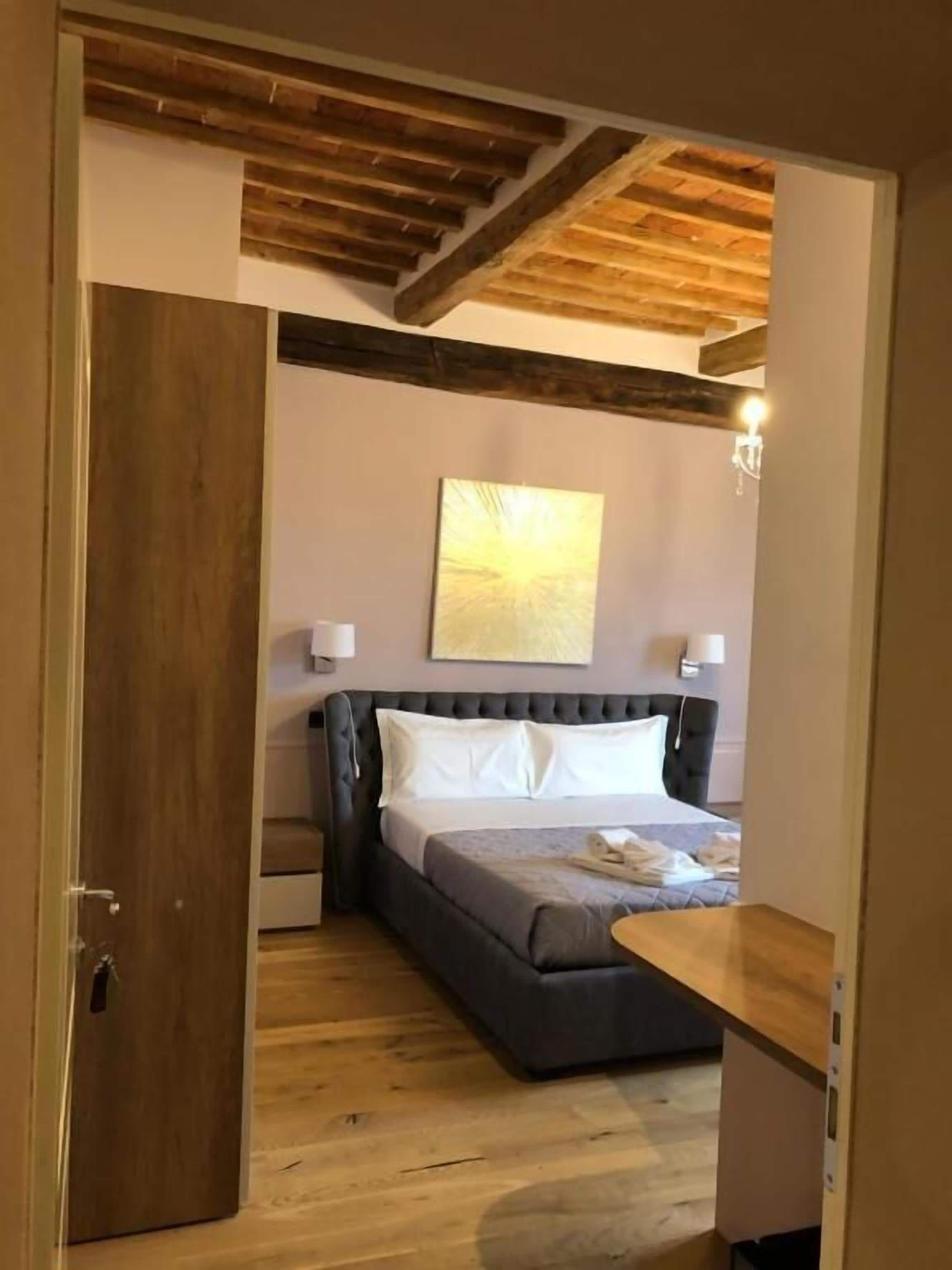 A bedroom with a bed, bedside lamps, a wooden ceiling, and a painting on the wall.