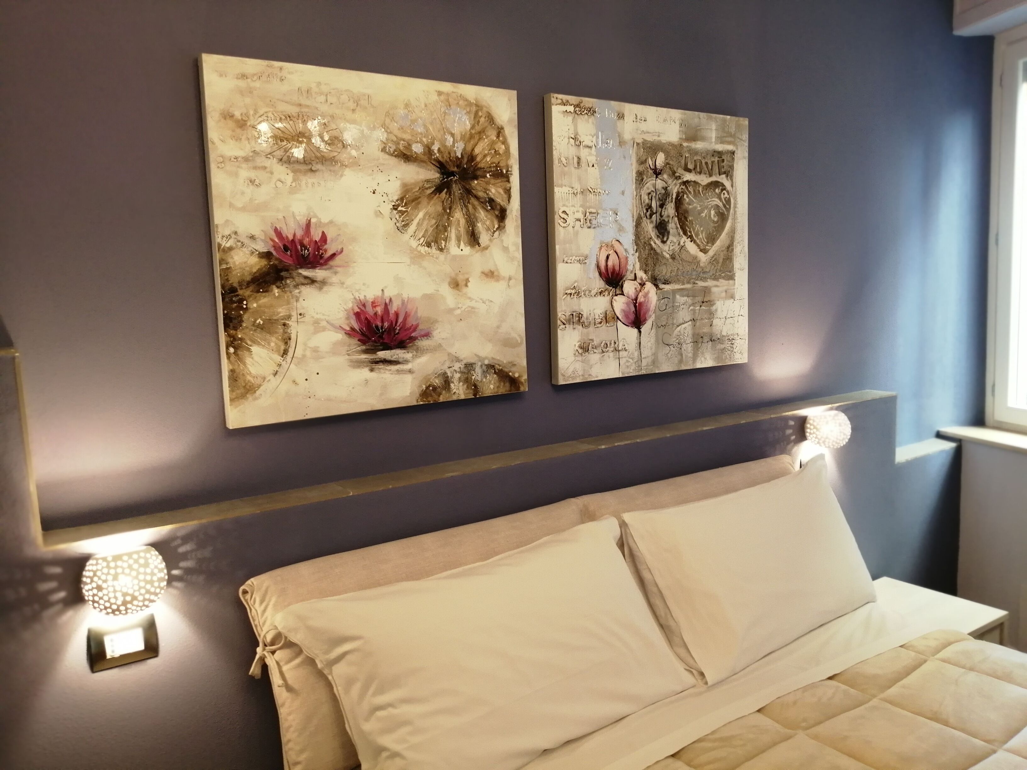 A bedroom with a bed, two wall art pieces, and a bedside lamp.