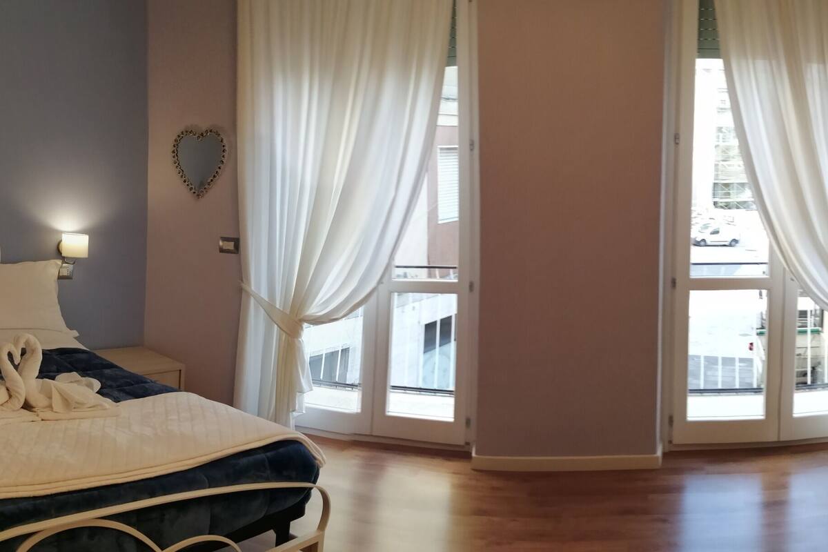 A bedroom with a bed, a nightstand, a green sofa, and a window with curtains.