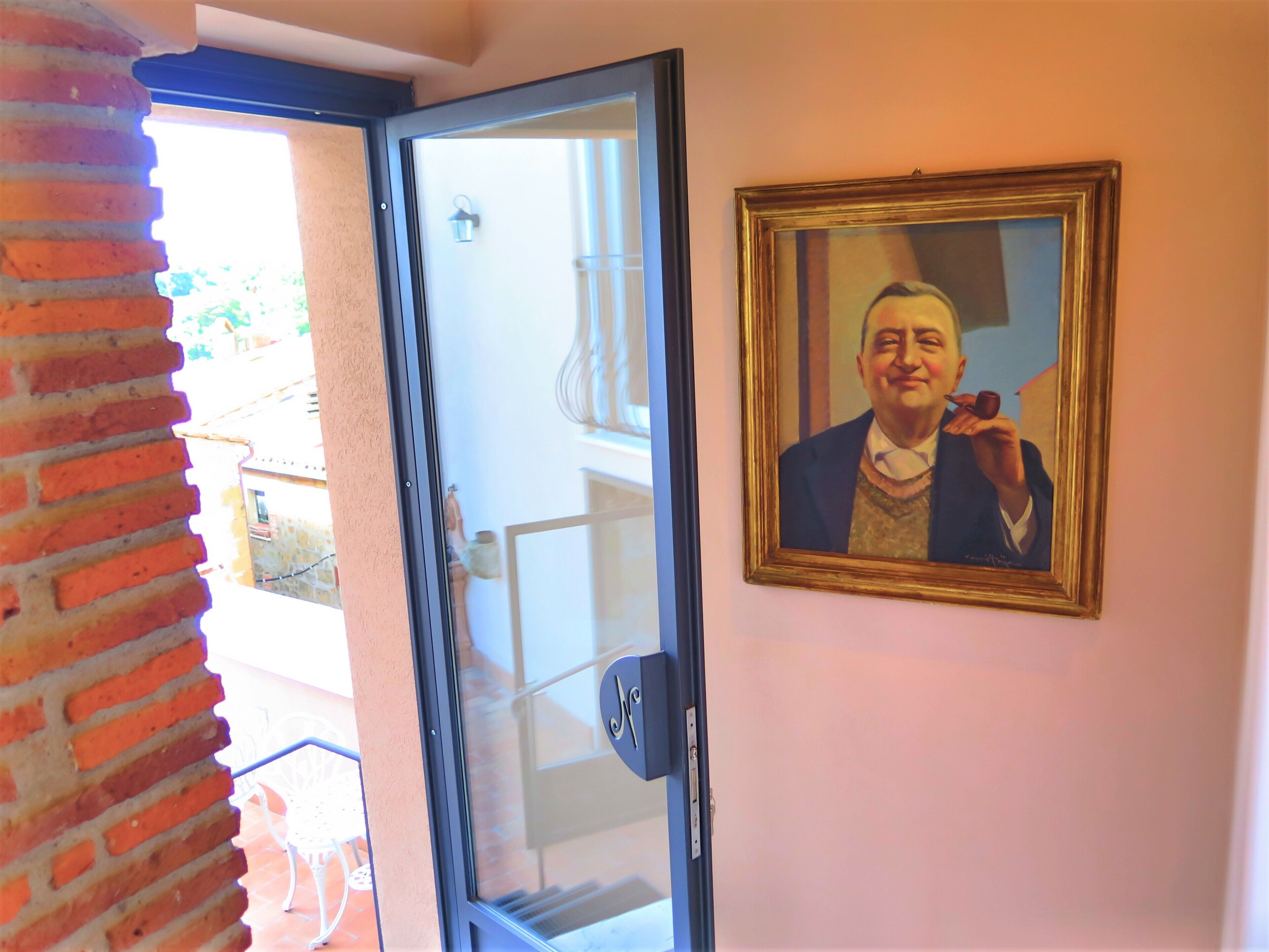 Una stanza con una porta in vetro che dà su un balcone, un ritratto incorniciato al muro e una colonna in mattoni.