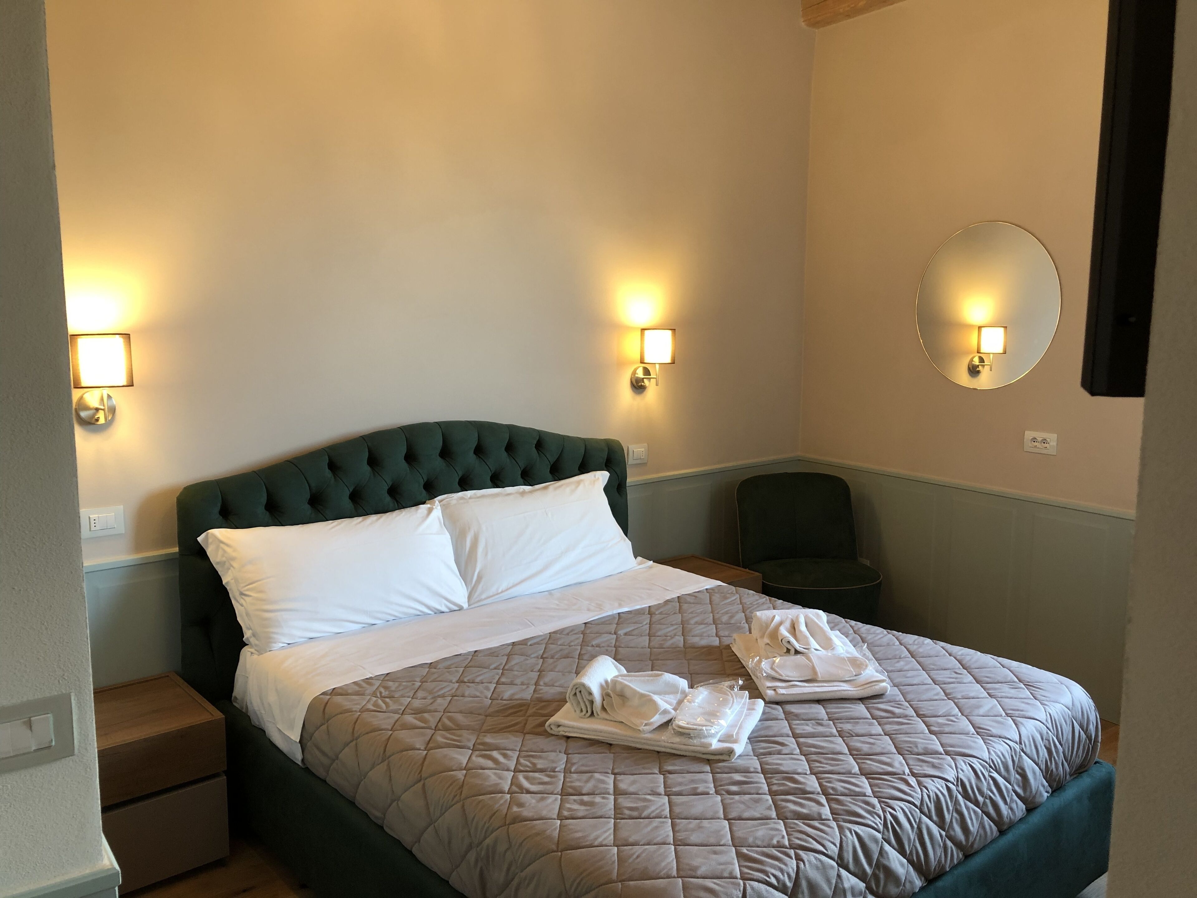 Hotellihuone, jossa on suuri sänky, kaksi yöpöytää, tuoli ja seinään kiinnitetyt valaisimet.