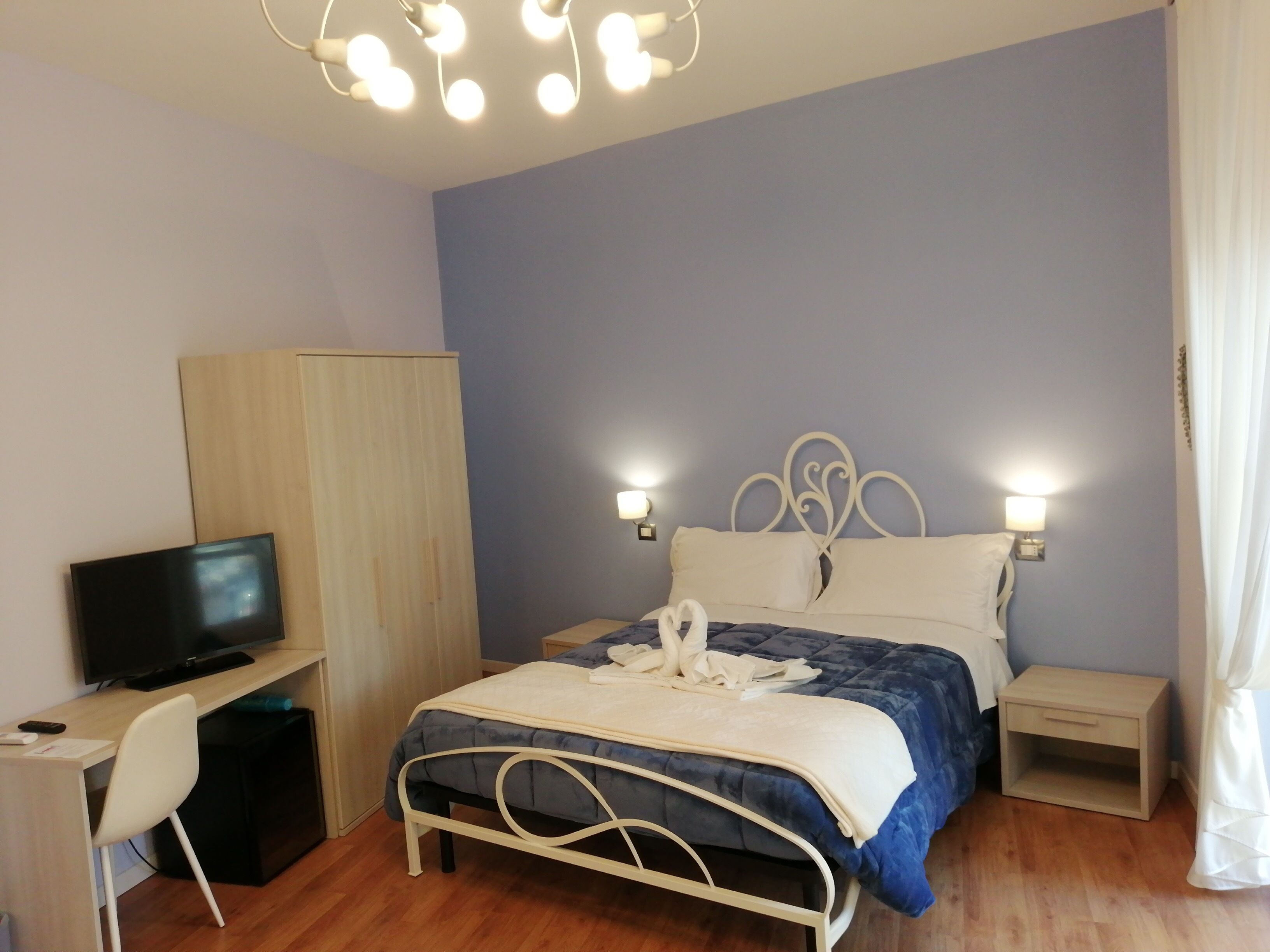 A bedroom with a bed, bedside tables, a TV, a wardrobe, and a desk.