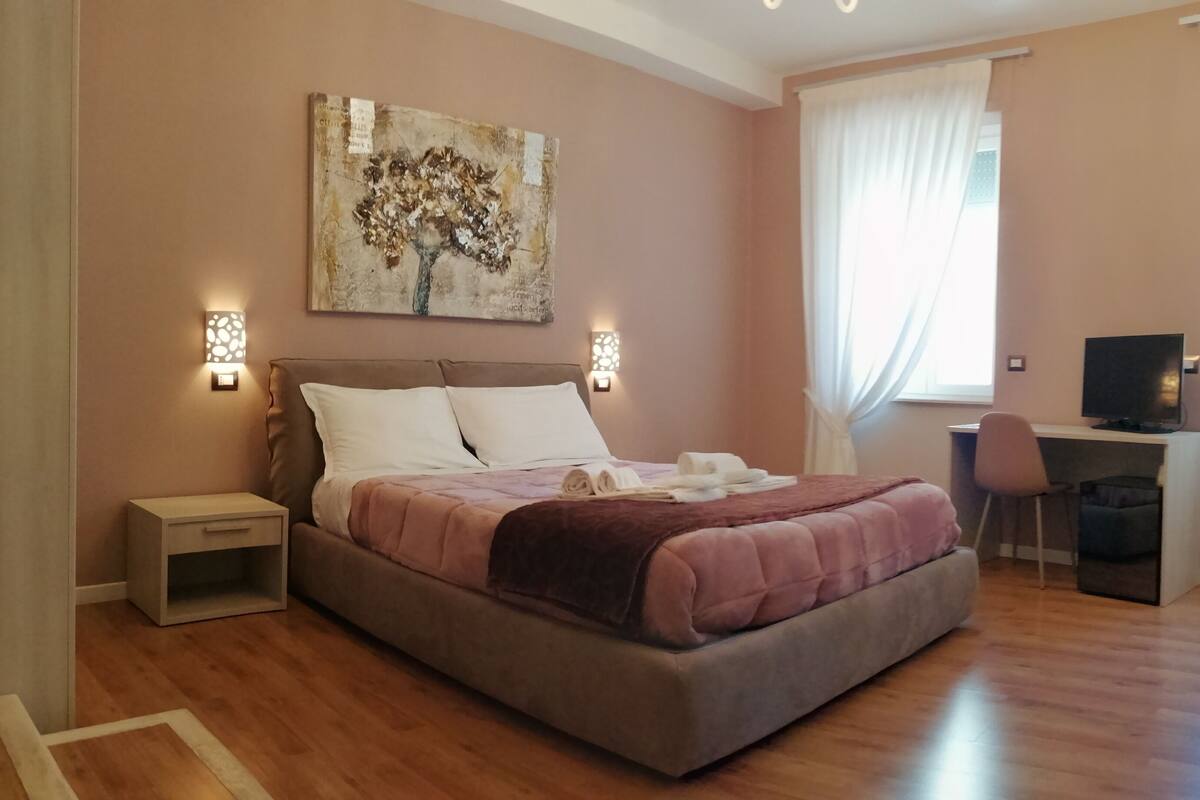 A bedroom with a bed, bedside tables, a desk, a chair, and a painting on the wall.
