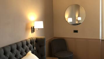 A hotel room with a tufted headboard, a round mirror, a bedside lamp, a chair, and a neatly made bed with a quilted cover.