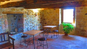 Una habitación rústica con paredes de piedra, una mesa de madera y cuatro sillas, un banco y una planta en maceta cerca de una ventana.