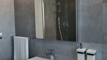 Ein modernes Badezimmer mit einem großen Spiegel, einem weißen Waschbecken und einer Dusche.