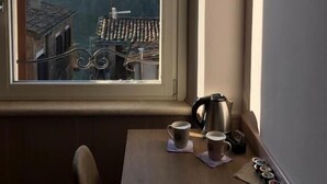 Una habitación con un ventanal grande que da a un paisaje urbano, una mesa de madera con un hervidor y tazas, y una silla.