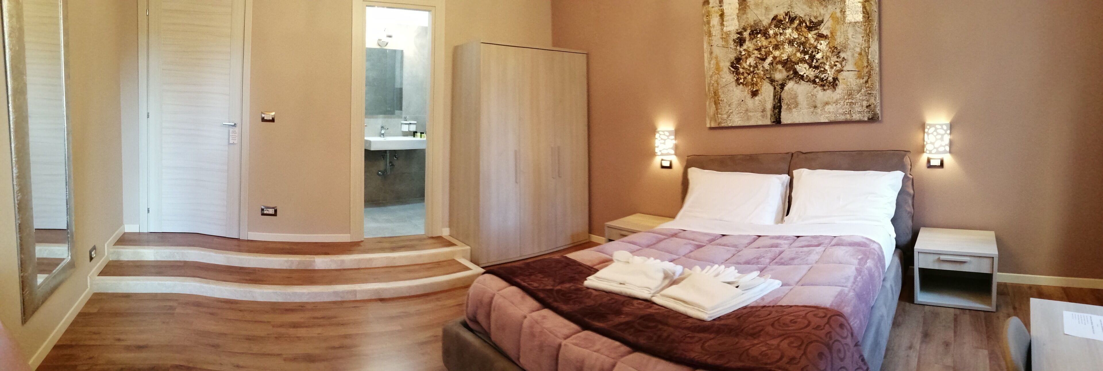 A hotel room with a bed, nightstands, a bathroom with a sink and mirror, and a staircase leading to another room.