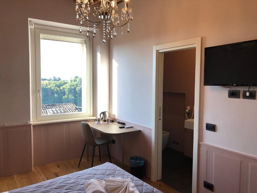 Un dormitorio con cama, escritorio, silla, televisión y ventana con vistas a árboles.