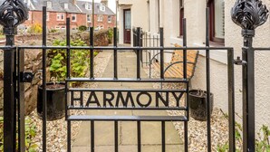 Una entrada con puerta metálica que muestra la palabra "HARMONY", un camino y una banca.