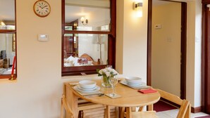 Un comedor con una mesa de madera dispuesta para dos personas, un espejo sobre la mesa y un reloj en la pared.