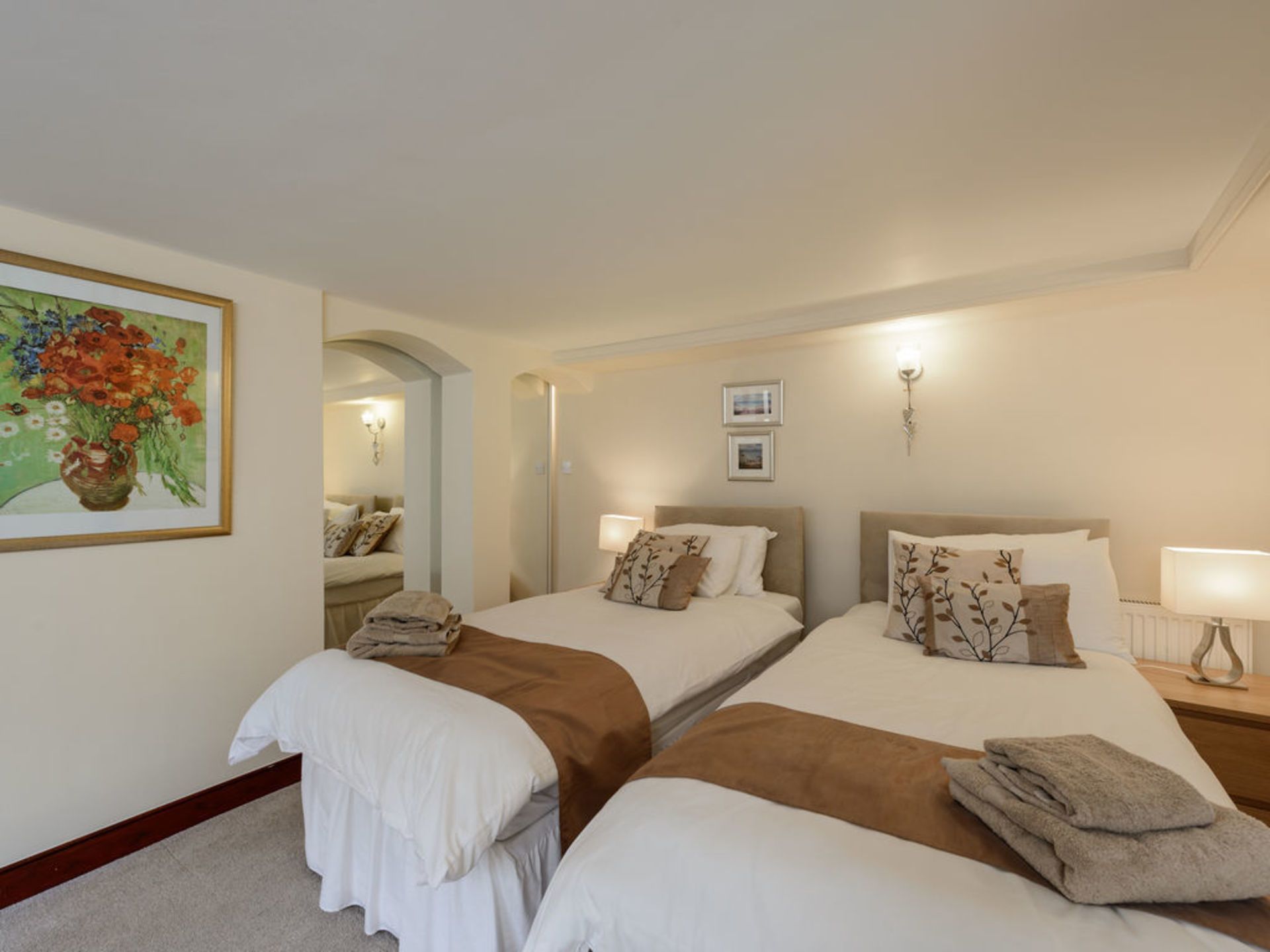 A hotel room with two beds, a painting of flowers on the wall, and a mirror.
