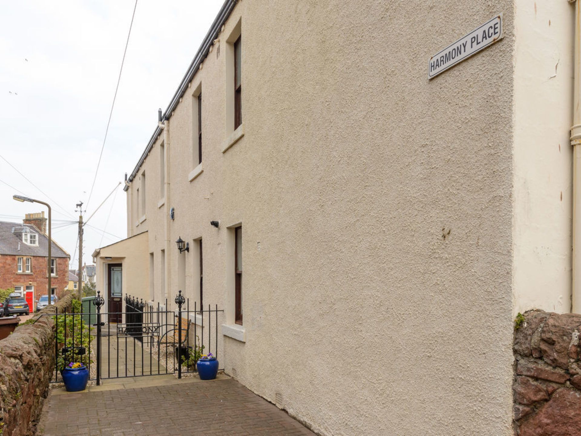 Une rue étroite bordée de maisons mitoyennes, avec un portail en métal et un lampadaire.
