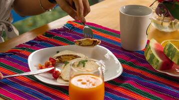 Una mesa con un posavasos tejido y de colores, un plato con comida, un vaso de jugo de naranja y una taza blanca.