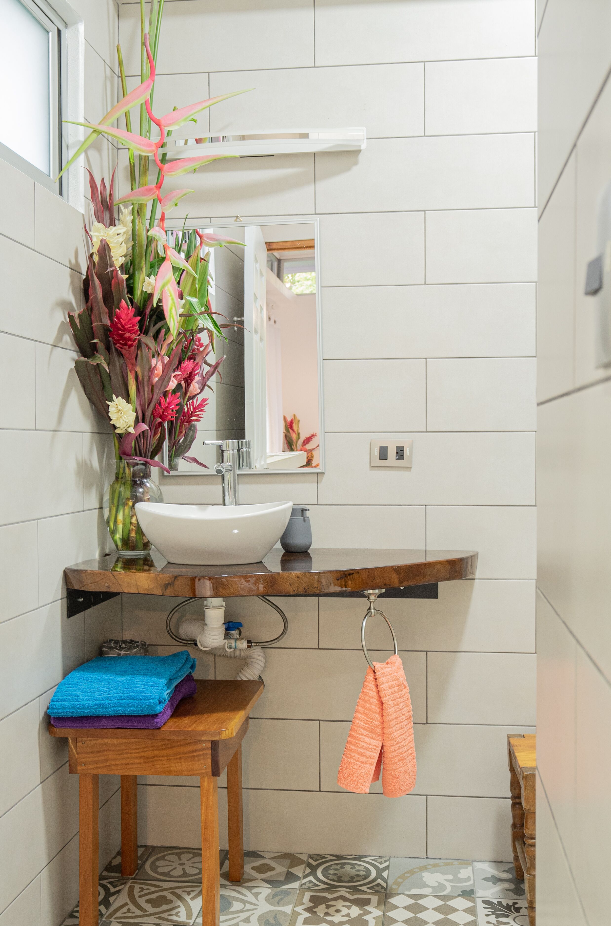 Ein Badezimmer mit weißem Waschbecken, einem Spiegel, einer Blumenvase und einem Handtuchhalter.