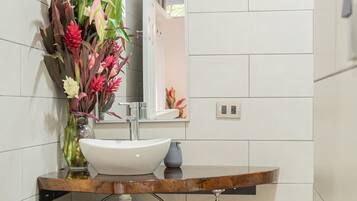 Ein Badezimmer mit weißem Waschbecken, einem Spiegel, einer Blumenvase und einem Handtuchhalter.
