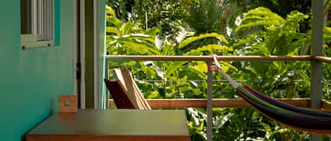 Une table et un banc en bois sur un balcon, avec un hamac, donnant sur une végétation luxuriante.