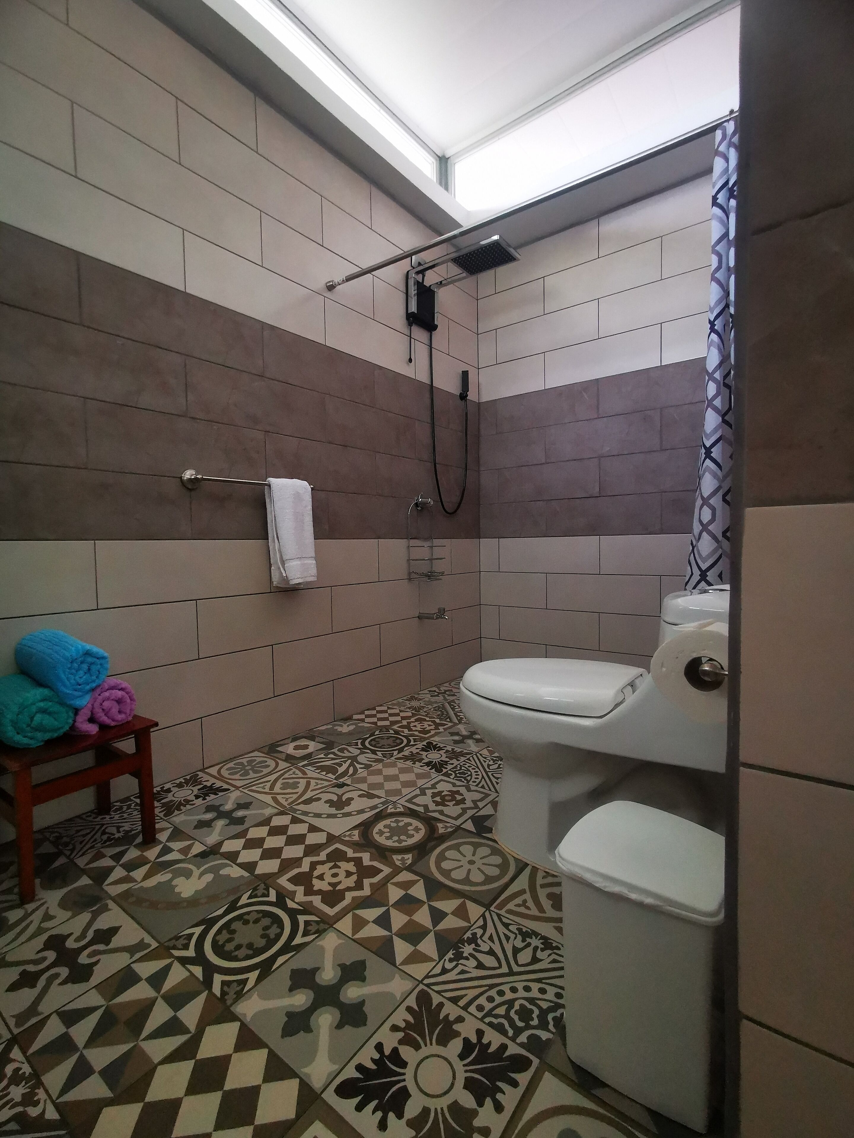 Un baño con ducha, inodoro y baldosas estampadas.