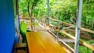 A wooden table and benches under a covered area with a view of a garden.