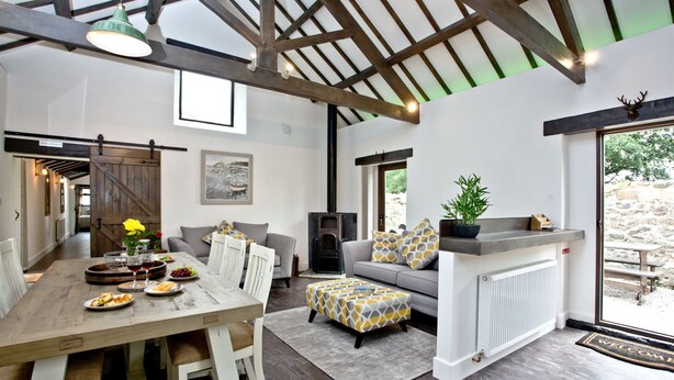 A spacious living area with a wooden dining table, grey sofa, and a fireplace.