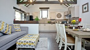 A modern kitchen with a dining area, featuring a grey sofa, patterned ottoman, and white chairs.