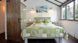 A bedroom with a bed, bedside tables, a wooden door, a window, and a painting on the wall.
