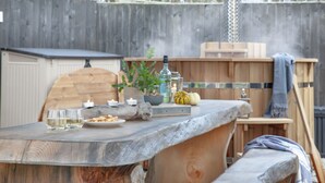 A rustic outdoor dining area with a wooden table, candles, and a bottle of olive oil.