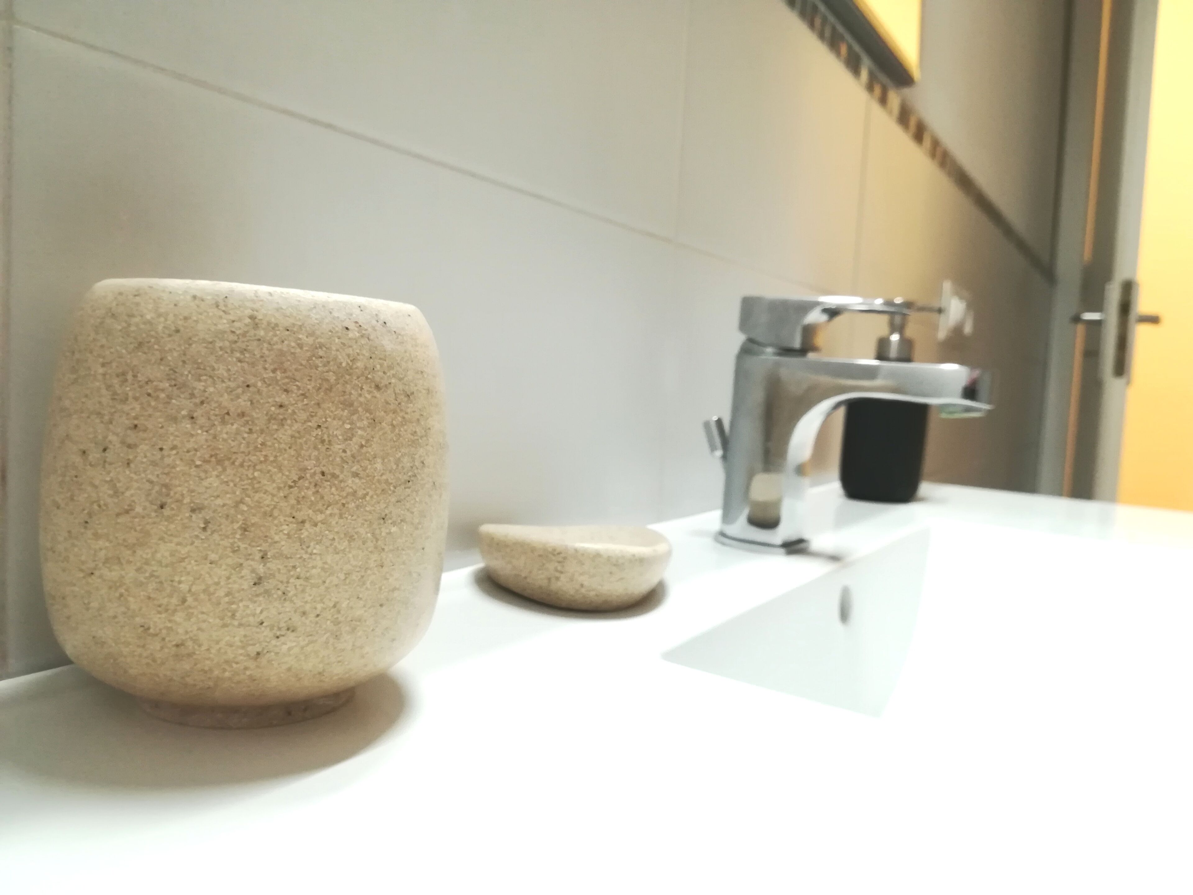 A bathroom with a white countertop, a stone mug, and a small stone bowl.