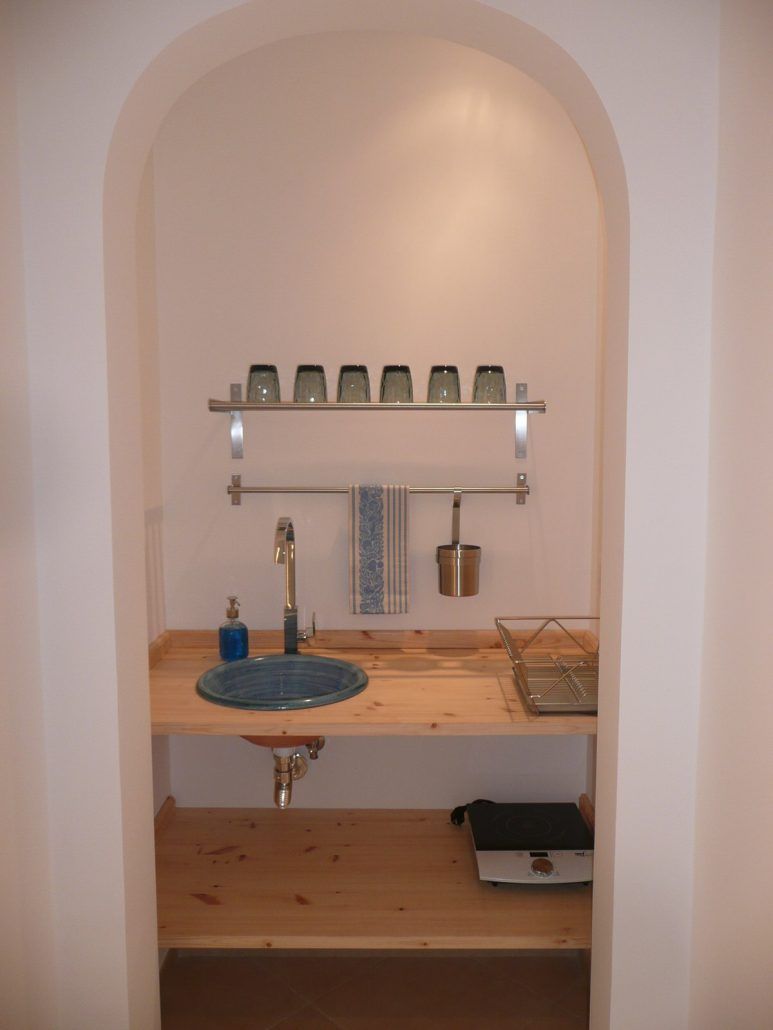 Ein kleines Badezimmer mit einem Holzwaschtisch, einem Glasbecken und einem Regal für verschiedene Pflegeprodukte.