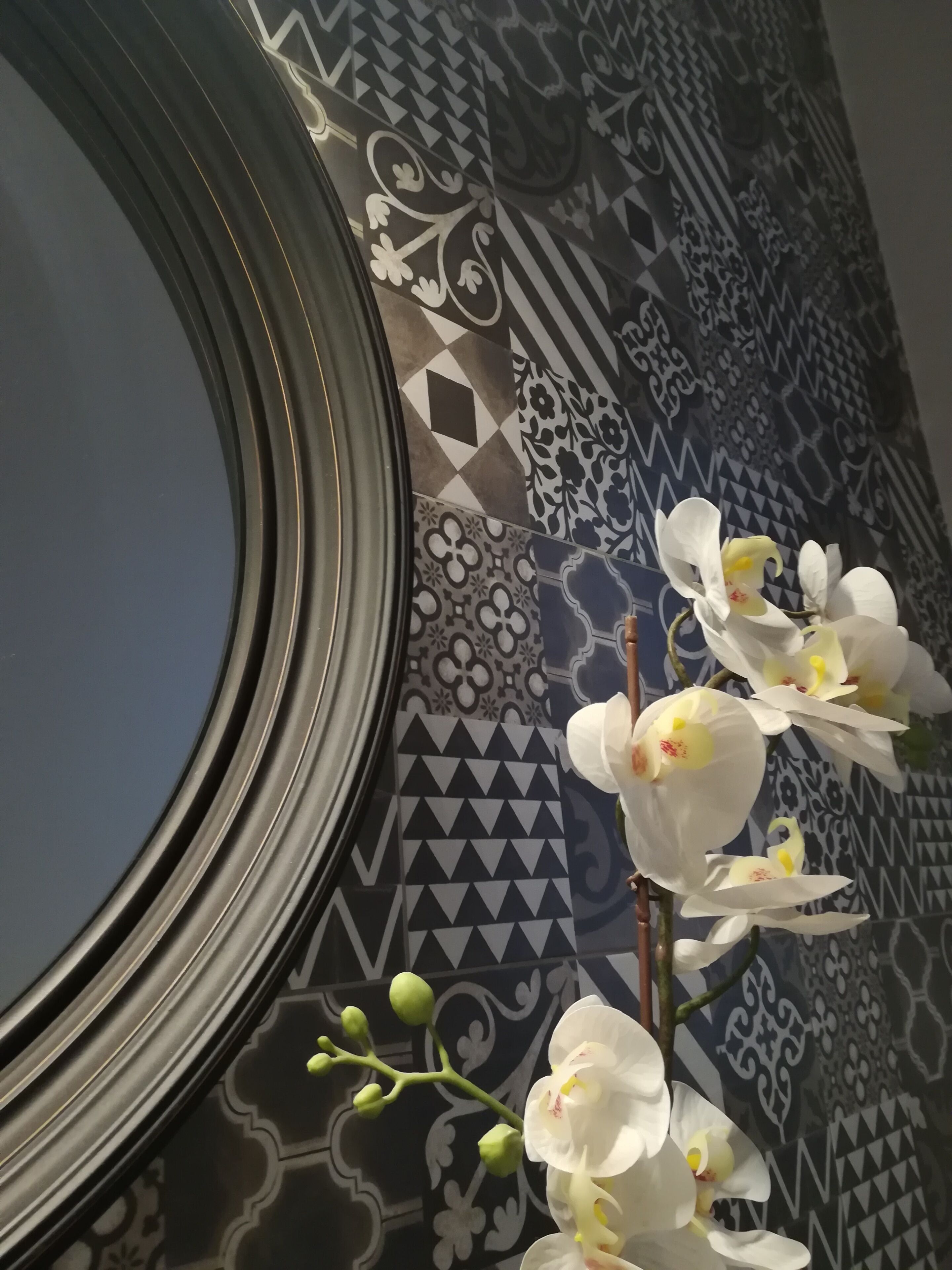 A bathroom with a large mirror, patterned tiles, and white orchids.