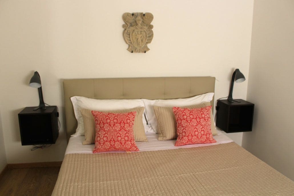A neatly made bed with a beige headboard, two bedside tables with lamps, and a decorative wall piece above the bed.