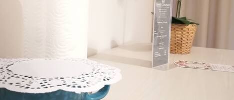 A bathroom with a white towel dispenser, a blue ceramic sink with a lace doily, a wooden tray, and a sign listing amenities like Wi-Fi and a self-service checkout.