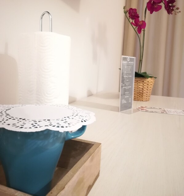 A bathroom with a white towel dispenser, a blue ceramic sink with a lace doily, a wooden tray, and a sign listing amenities like Wi-Fi and a self-service checkout. - I Santi Coronati Bed & Breakfast (Syracuse)