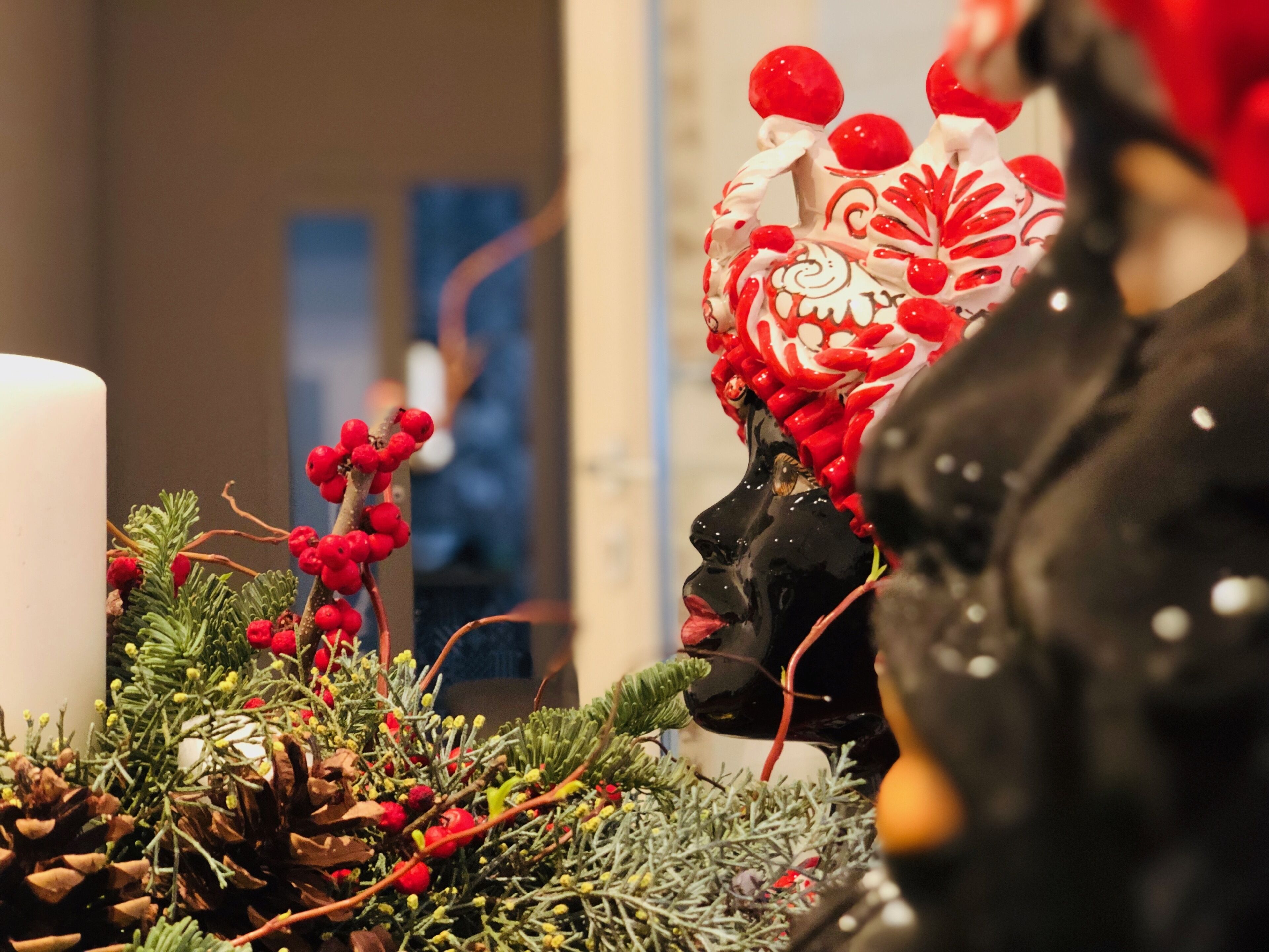 A festive display with a white candle, red berries, and a decorative figure.