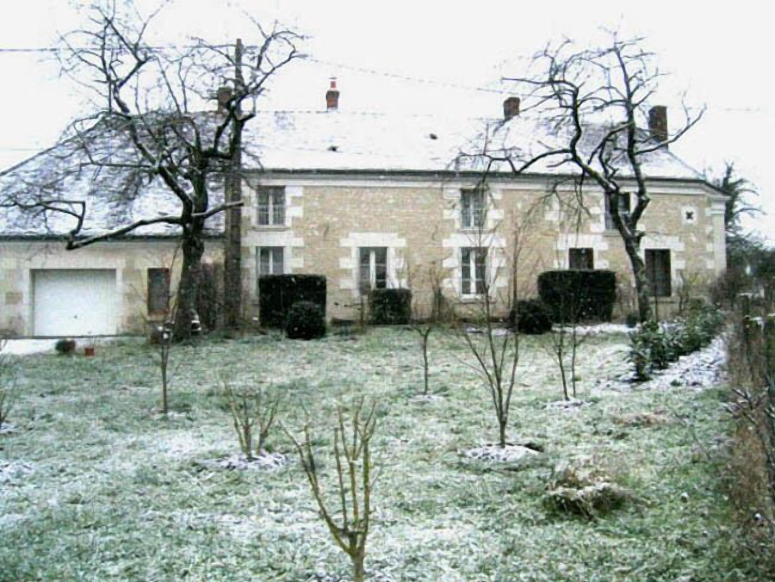 A two-story stone building with a garage, surrounded by a snow-covered lawn and leafless trees.