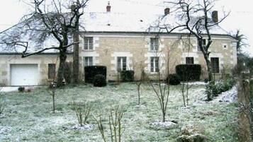 A two-story stone building with a garage, surrounded by a snow-covered lawn and leafless trees.