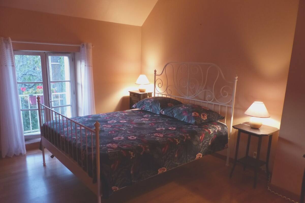 A bedroom with a bed, two bedside tables with lamps, a window with curtains, and a door.