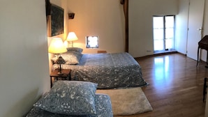 A room with two beds, each with patterned bedding and a bedside lamp. There is a window with a view of the outside, and a door leading to another room. - La Lézardière (Épeigné-les-Bois)