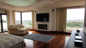 A modern bedroom with a large bed, a sofa, a TV, and a fireplace.