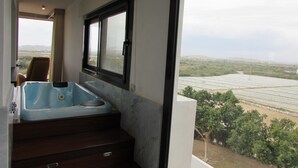 A bathroom with a large bathtub, a window, and a view of a green landscape.