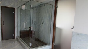 A modern bathroom with a glass-enclosed shower, marble flooring, and a wooden door.