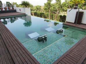 Una piscina infinita rectangular con borde de azulejos, rodeada por una terraza de madera.