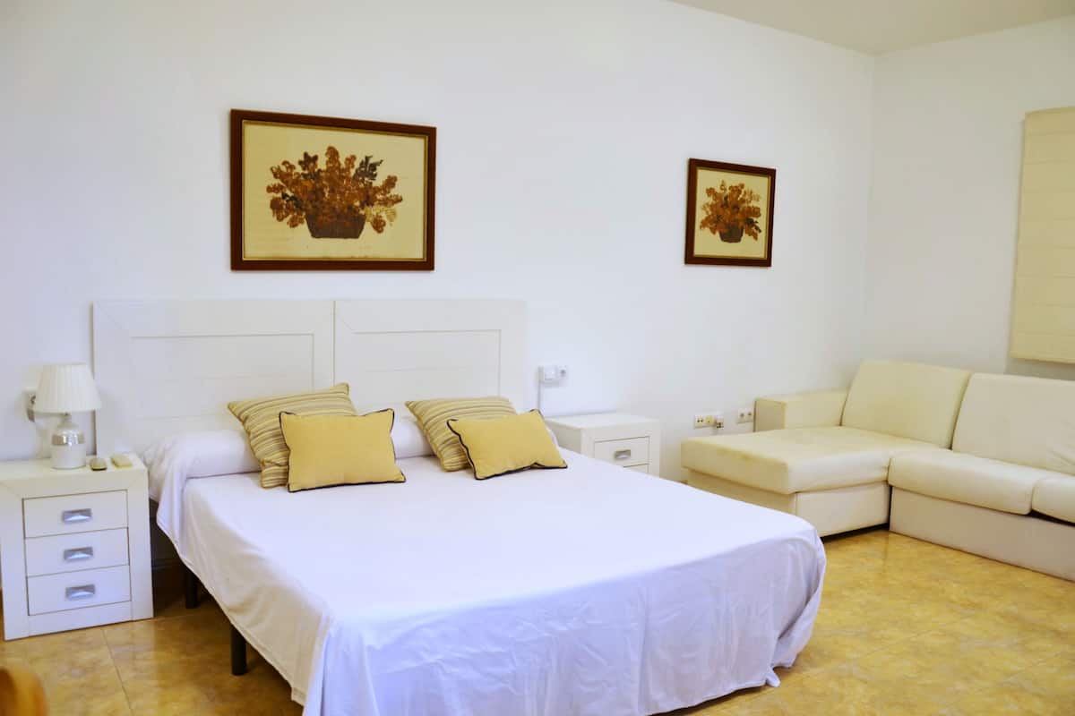 A bedroom with a large bed, two bedside tables, a nightstand, a sofa, and two framed pictures on the wall.